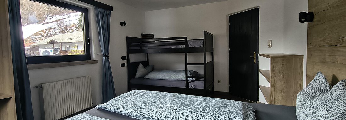 A modern room with a double bed and a bunk bed. The room has a window with a view outside and is decorated in neutral colors. - Gästehaus Hermann Arnold - Sölden