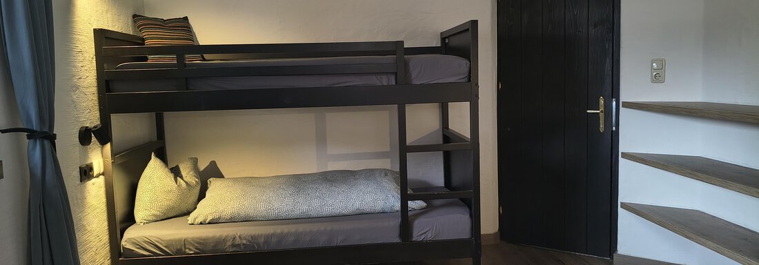 A simple bedroom with a bunk bed and a single bed. There is a wooden floor and modern furnishings. - Gästehaus Hermann Arnold - Sölden
