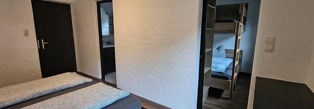 A modern room with two single beds and a wooden floor. In the background, an adjoining room with bunk beds is visible. - Gästehaus Hermann Arnold - Sölden