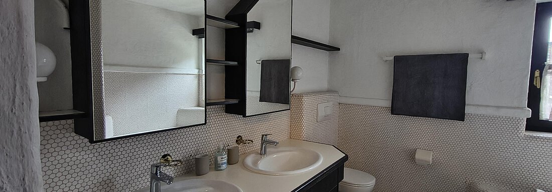 A modern bathroom with two sinks and large mirrors. The walls are bright, and the decor looks simple and functional. - Gästehaus Hermann Arnold - Sölden