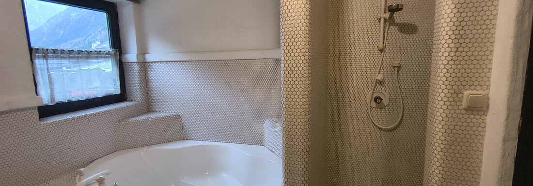 A modern bathroom with a shower and a bathtub. There is a window that lets in natural light. - Gästehaus Hermann Arnold - Sölden