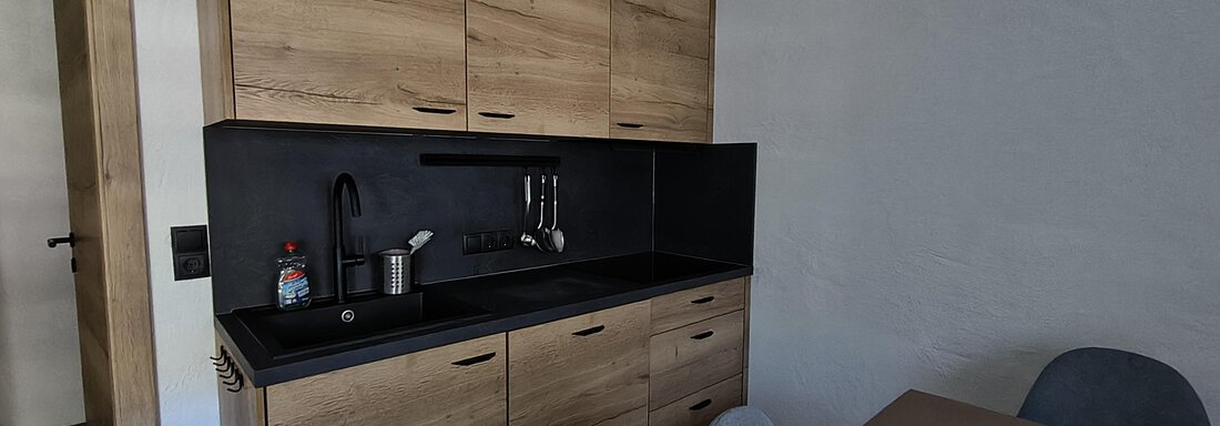 A modern kitchen made of wood with a black body. The table and chairs are simply designed and create an inviting atmosphere. - Gästehaus Hermann Arnold - Sölden