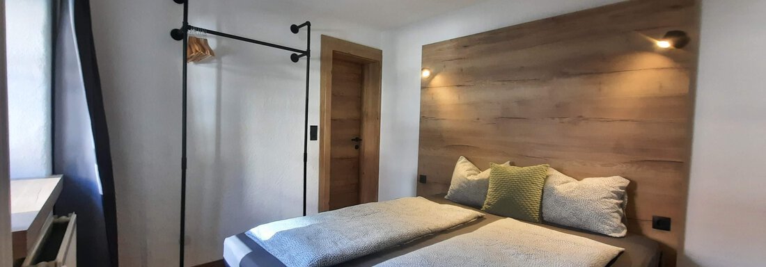 A modern bedroom with a double bed and wood paneling. There is a coat rack and cozy lighting. - Gästehaus Hermann Arnold - Sölden