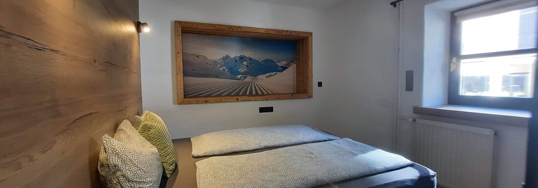 A cozy bedroom with a modern bed and beautiful wall decoration. The room is bright and welcoming with a window that lets in plenty of daylight. - Gästehaus Hermann Arnold - Sölden