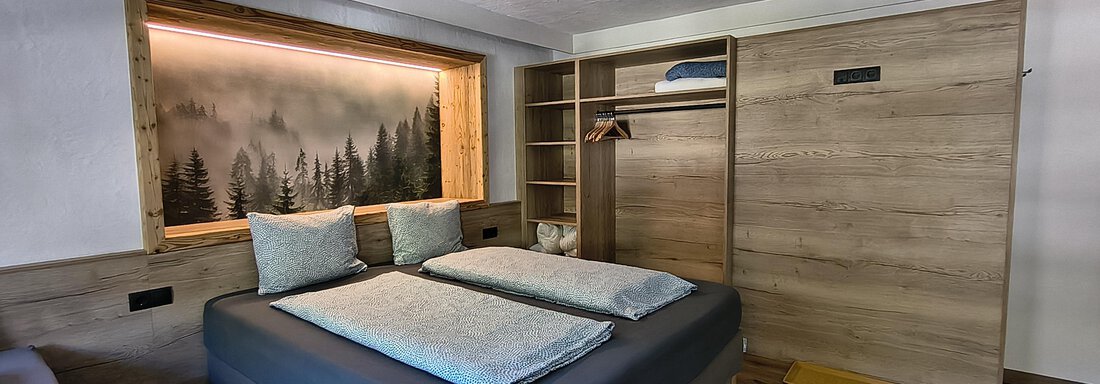 A modern bedroom with two beds and a large window.  
On the wall, there is a cozy forest motif. - Gästehaus Hermann Arnold - Sölden