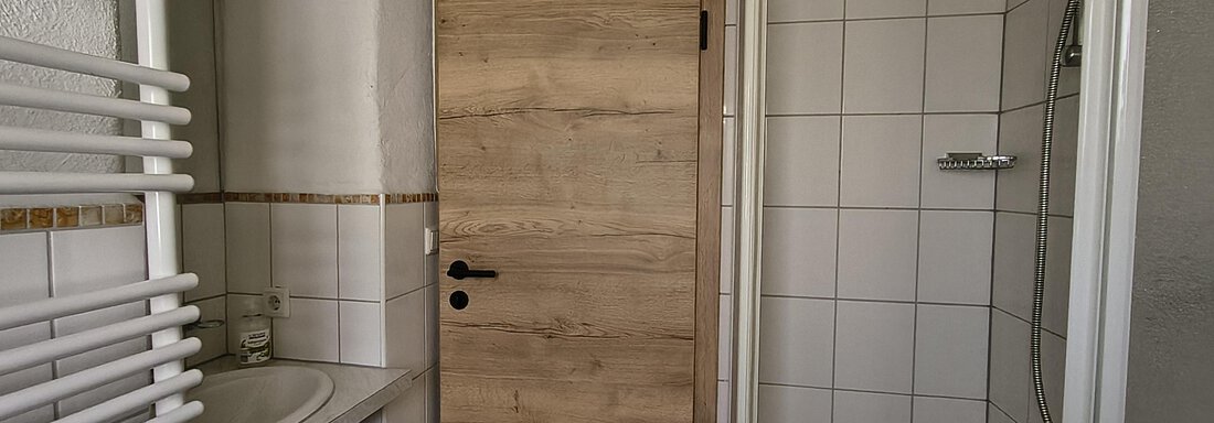 A modern bathroom with a sink, a shower, and a wooden cabinet. The walls are tiled with white tiles and there is a towel warmer. - Gästehaus Hermann Arnold - Sölden
