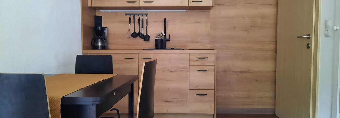 A modern kitchen unit made of wood with a dining table and chairs. The room is brightly and friendly furnished. - Gästehaus Hermann Arnold - Sölden