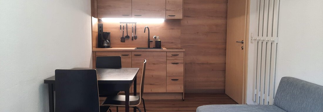A modern kitchen unit in a bright room with a dining table and chairs. In the foreground, there are two comfortable sofas. - Gästehaus Hermann Arnold - Sölden