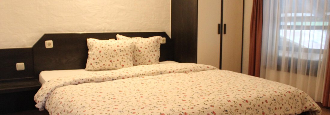 A cozy bedroom with a large bed and colorful bed covers. The walls are bright, and there is a wardrobe as well as a window with curtains. - Gästehaus Hermann Arnold - Sölden