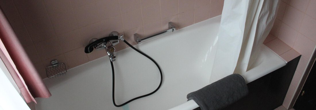 A bathroom bathtub with a shower curtain and a towel. The walls are in a soft pink. - Gästehaus Hermann Arnold - Sölden
