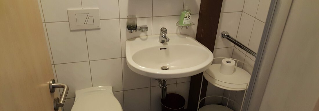 A small bathroom with a toilet and a sink. There are bright wall tiles and practical shelves. - Gästehaus Hermann Arnold - Sölden