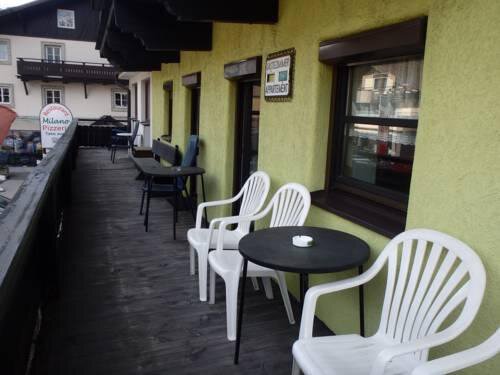 A balcony with white plastic chairs and tables. The area has a yellow wall and a view of a street. - Gästehaus Hermann Arnold - Sölden