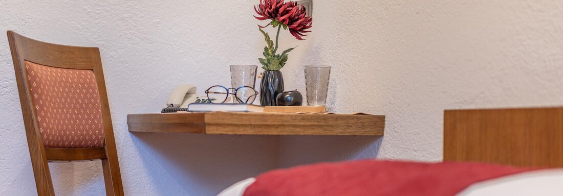 Ein gemütliches Zimmer mit einem Holzstuhl und einem kleinen Tisch. Auf dem Tisch stehen eine Blume und einige persönliche Gegenstände. - Gästehaus Maier - Sölden
