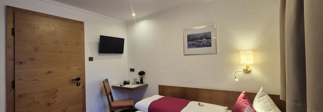 Ein gemütliches Hotelzimmer mit einem Einzelbett und einem Stuhl. Das Zimmer ist hell beleuchtet und hat einen Fernseher sowie große Fenster. - Gästehaus Maier - Sölden