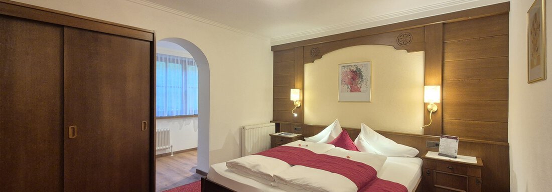Ein gemütliches Schlafzimmer mit einem großen Doppelbett und modernem Fernseher. Der Raum ist warm eingerichtet und hat einen roten Teppich. - Gästehaus Maier - Sölden