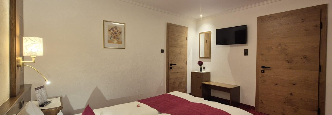 Ein gemütliches Schlafzimmer mit einem großen Doppelbett und modernem Fernseher. Der Raum ist warm eingerichtet und hat einen roten Teppich. - Gästehaus Maier - Sölden