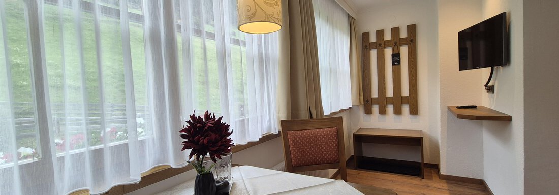 Lichtdurchfluteter Raum mit Sitzecke, Fernseher und Garderobe. - Gästehaus Maier - Sölden