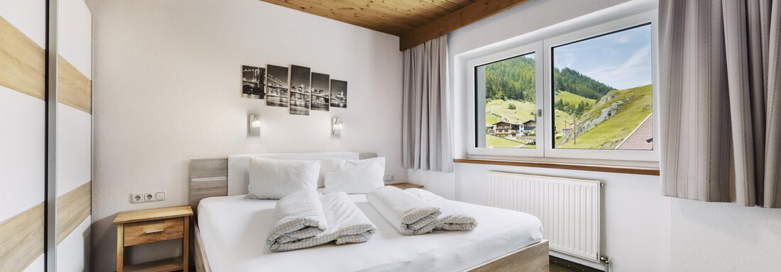 _F0A8073 Ein modernes Schlafzimmer mit einem großen Bett und frischen Handtüchern. Durch das Fenster ist eine grüne Landschaft zu sehen. - Gasthof Granstein - Sölden