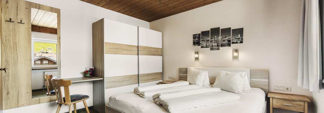 Ein modernes Schlafzimmer mit einem großen Bett und Holzelementen. Es gibt einen Schreibtisch und einen Stuhl, sowie einen eingebauten Kleiderschrank. - Gasthof Granstein - Sölden