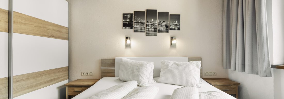 Ein modernes Schlafzimmer mit einem Doppelbett und einer Holzdecke. An der Wand hängt ein Bild mit Stadtansicht, und es gibt helle Vorhänge. - Gasthof Granstein - Sölden