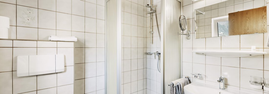 Ein modernes Badezimmer mit einer Duschkabine, einem Waschbecken und einem großen Spiegel. Die Wände sind gefliest und die Decke ist aus Holz. - Gasthof Granstein - Sölden
