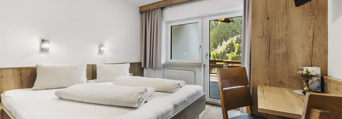 Ein modernes Hotelzimmer mit einem Doppelbett und zwei Decken. Das Zimmer hat große Fenster, die auf einen Balkon mit Blick auf die Berge führen. - Gasthof Granstein - Sölden