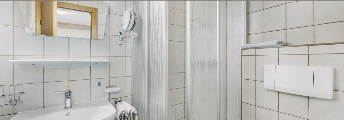 Ein modernes Badezimmer mit einer Dusche, einem Waschbecken und einem großen Spiegel. Die Wände sind mit hellen Fliesen ausgekleidet, was für eine freundliche Atmosphäre sorgt. - Gasthof Granstein - Sölden