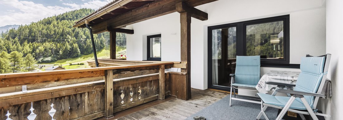 Ein gemütlicher Balkon mit Holzverkleidung und zwei Stühlen. Im Hintergrund sind grüne Hügel und ein klarer Himmel zu sehen. - Gasthof Granstein - Sölden