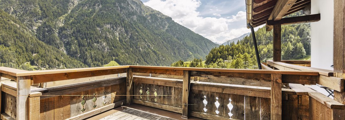 Eine Holzterrasse mit Blick auf majestätische Berge und eine grüne Landschaft. Der Himmel ist teilweise bewölkt und vermittelt eine ruhige Atmosphäre. - Gasthof Granstein - Sölden