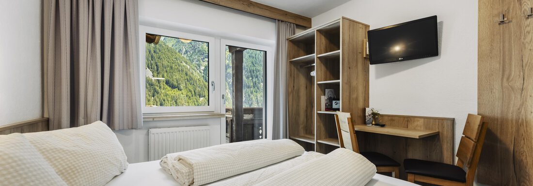 Ein modernes Zimmer mit zwei Einzelbetten, einem Schreibtisch und einem Fernseher. Durch das Fenster ist eine schöne Aussicht auf die Berge sichtbar. - Gasthof Granstein - Sölden
