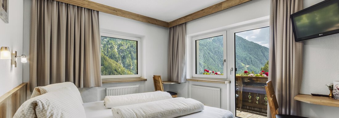 Ein helles Schlafzimmer mit einem Doppelbett und Aussicht auf die Berge. Es gibt einen kleinen Balkon und einen Fernseher an der Wand. - Gasthof Granstein - Sölden