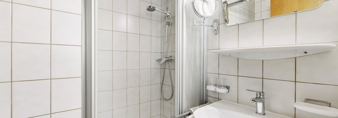 Ein modernes Badezimmer mit einer Duschkabine und einem Waschbecken. Die Wände sind mit weißen Fliesen gefliest und es gibt einen Spiegel über dem Waschbecken. - Gasthof Granstein - Sölden