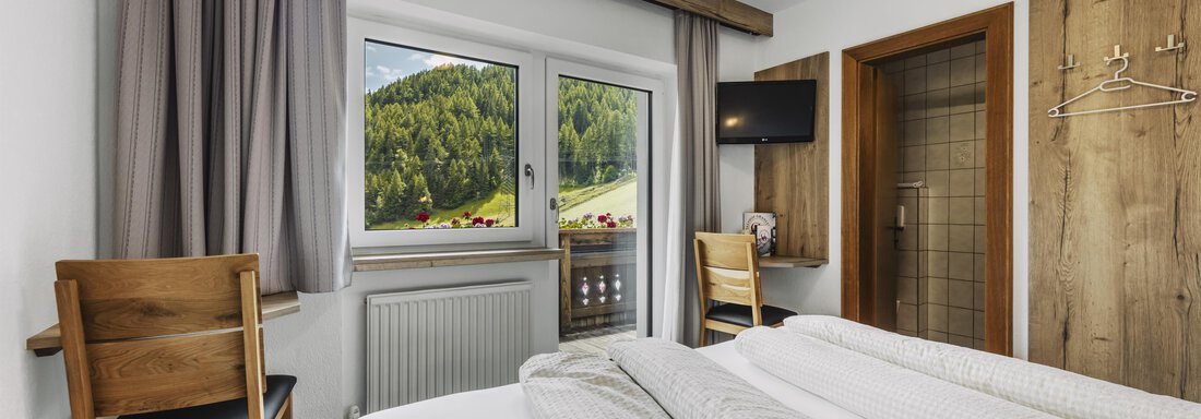 Ein gemütliches Zimmer mit zwei Betten und Holzdekor. Große Fenster bieten einen Blick auf die grüne Umgebung. - Gasthof Granstein - Sölden