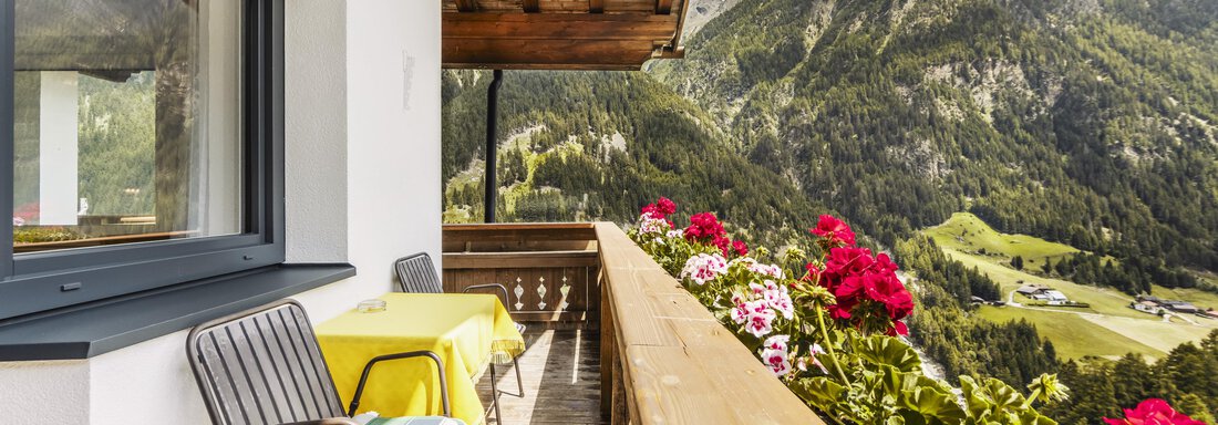Ein Balkon mit Blick auf grüne Berge und blühende Blumen. Zwei Stühle und ein Tisch laden zum Entspannen ein. - Gasthof Granstein - Sölden