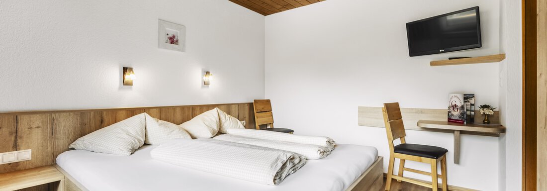 Ein gemütliches Schlafzimmer mit einem Doppelbett und Holzverkleidung. Im Raum befinden sich ein Tisch, Stühle und ein Fernseher an der Wand. - Gasthof Granstein - Sölden