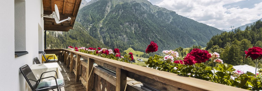 Ein Balkon mit bunten Blumen und zwei Stühlen. Im Hintergrund sind Berge und ein blauer Himmel zu sehen. - Gasthof Granstein - Sölden