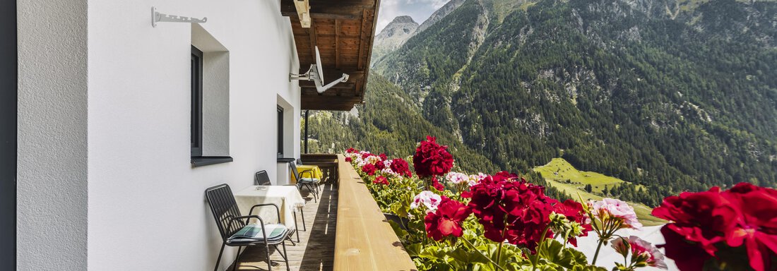 Ein Balkon mit Blumen und Blick auf die Berge. Die Umgebung ist grün und bewaldet, unter einem klaren Himmel. - Gasthof Granstein - Sölden