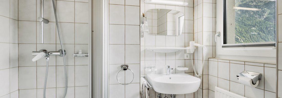 Ein modernes Badezimmer mit weißen Fliesen und einer Dusche. Es gibt ein Waschbecken, einen Spiegel und ein Fenster mit Ausblick. - Gasthof Granstein - Sölden