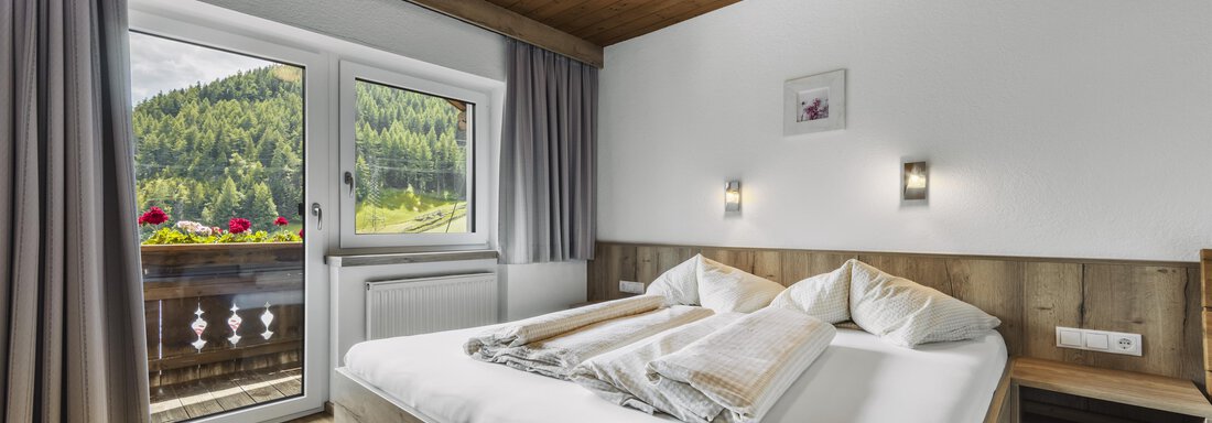 Ein helles und gemütliches Schlafzimmer mit Holzdecke und moderner Einrichtung. Der Balkon bietet einen schönen Blick auf die umliegende Natur. - Gasthof Granstein - Sölden