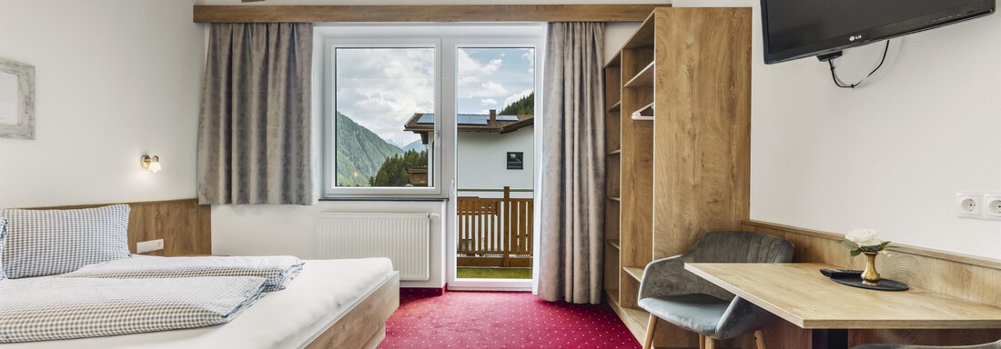 Ein helles Hotelzimmer mit Holzmöbeln und einem großen Fenster. Es gibt ein Bett, einen Tisch und einen Fernseher. - Gasthof Granstein - Sölden