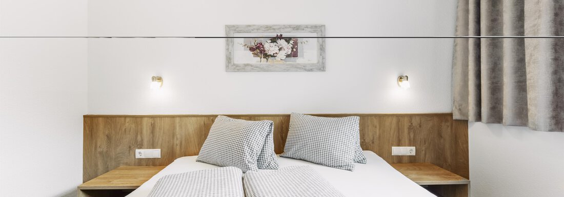 Ein modernes Schlafzimmer mit zwei Einzelbetten und grauen Kissen. Die Wände sind schlicht und es gibt eine Gardine sowie Wandleuchten. - Gasthof Granstein - Sölden