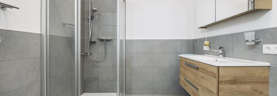 Ein modernes Badezimmer mit einer klaren Duschkabine und einem Holzwaschtisch. Die Wände sind in neutralen Grautönen gehalten, was einen eleganten Look verleiht. - Gasthof Granstein - Sölden