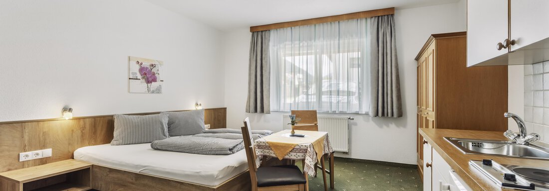 _F0A8297 Ein gemütliches Zimmer mit einem Doppelbett und einer kleinen Küchenzeile. Der Raum ist hell und freundlich mit einem Tisch und Stühlen sowie einem Fenster, das Tageslicht hereinlässt. - Gasthof Granstein - Sölden