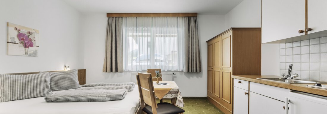 Ein einfaches Zimmer mit zwei Einzelbetten und einem kleinen Küchenbereich. Große Fenster lassen viel Licht herein und sorgen für eine helle Atmosphäre. - Gasthof Granstein - Sölden