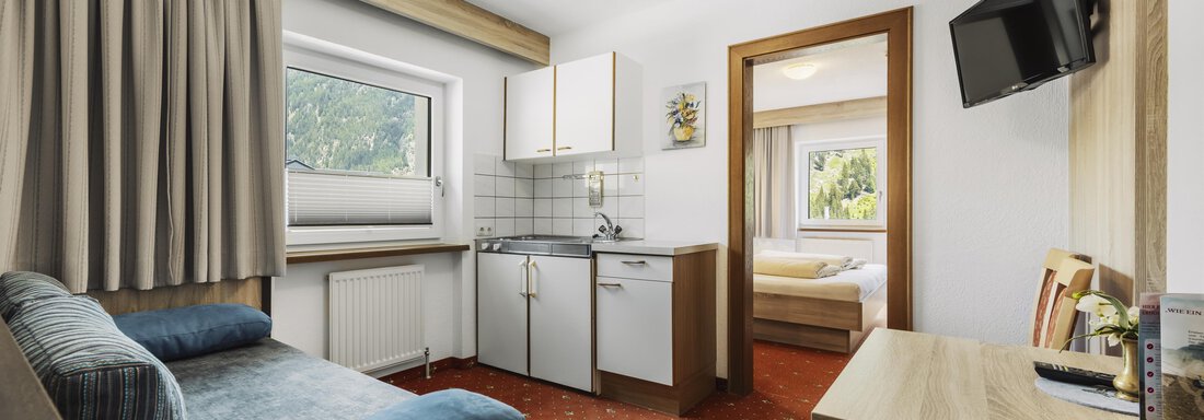 Ein gemütliches Zimmer mit einer kleinen Küchenzeile und einem Schlafbereich. Die Einrichtung ist einfach und praktisch, mit einem Fernseher an der Wand. - Gasthof Granstein - Sölden