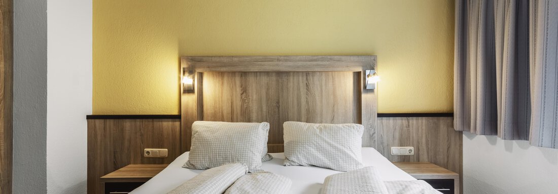 Ein gemütliches Schlafzimmer mit einem Doppelbett und zwei Kopfkissen. Die Wände sind gelb gestrichen und die Fenster sind mit grauen Vorhängen dekoriert. - Gasthof Granstein - Sölden