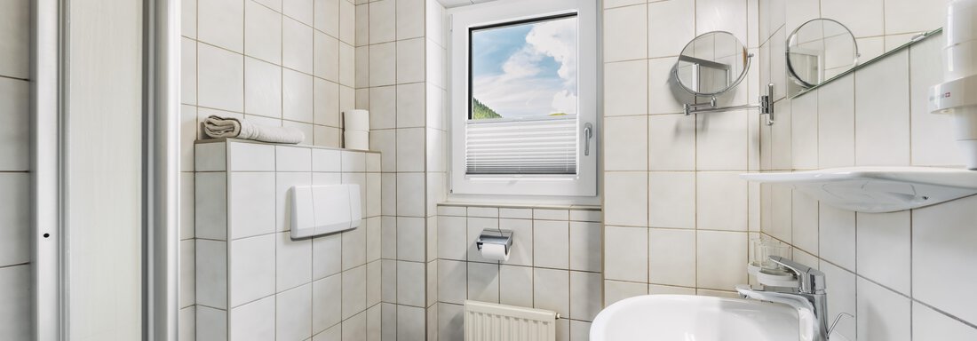 Ein modernes Badezimmer mit weißen Fliesen und Holzdecke. Es verfügt über ein Waschbecken, eine Toilette und ein Fenster mit Aussicht. - Gasthof Granstein - Sölden