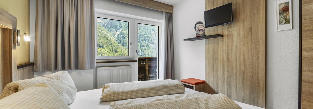 Ein gemütliches Hotelzimmer mit einem Doppelbett und zwei großen Kissen. Durch das Fenster sieht man eine grüne Landschaft. - Gasthof Granstein - Sölden