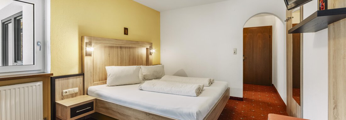 Ein helles Hotelzimmer mit einem Doppelbett und einem Fernseher. Die Wände sind in sanften Farben gehalten und es gibt einen komfortablen Sitzbereich. - Gasthof Granstein - Sölden