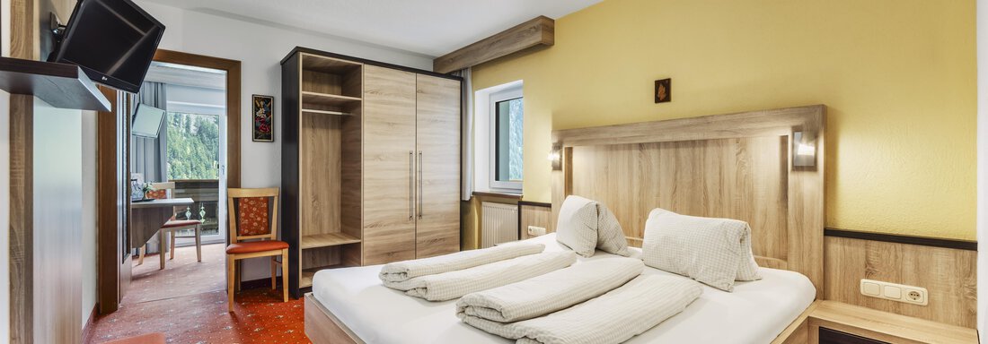 Ein gemütliches Hotelzimmer mit einem Doppelbett, sauberer Bettwäsche und modernem Mobiliar. An der Wand hängt ein Fernseher, und es gibt einen Zugang zu einem Balkon. - Gasthof Granstein - Sölden